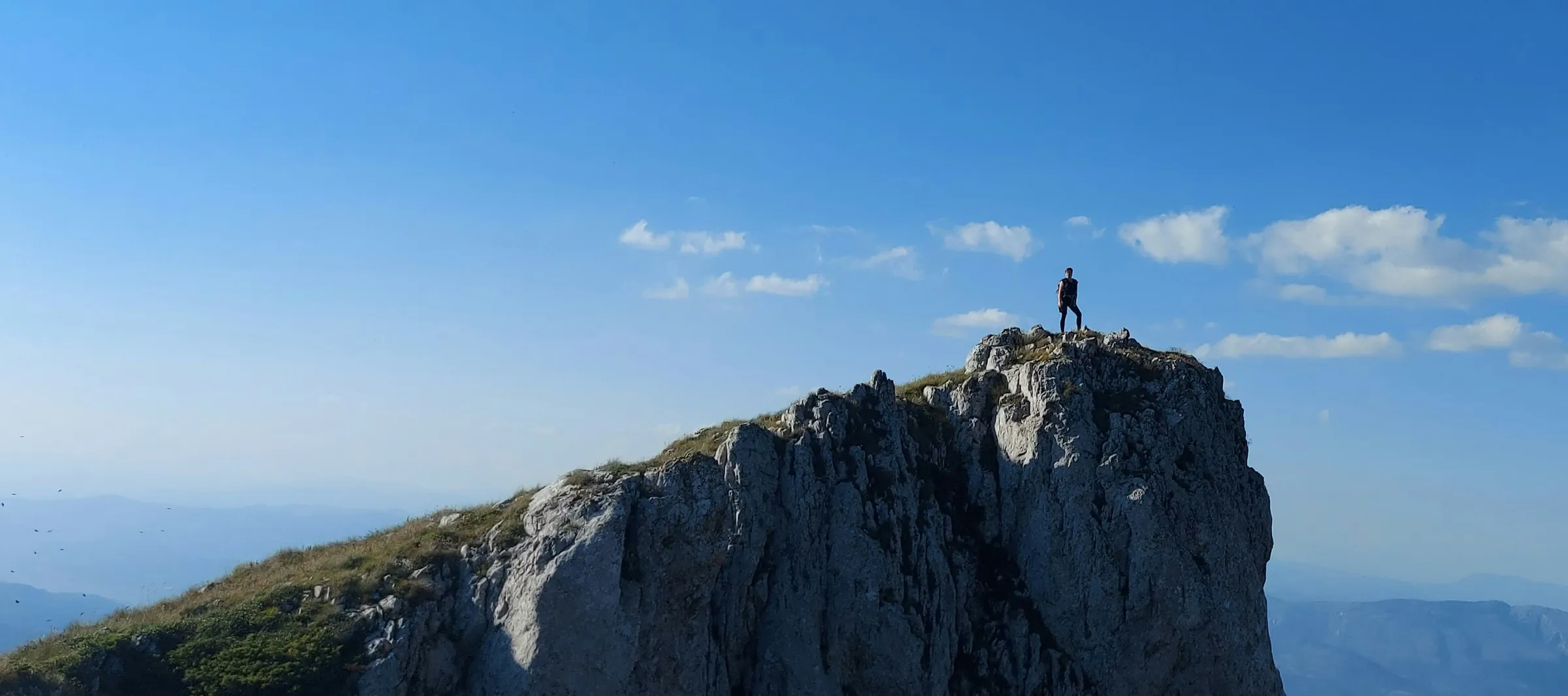 Hiker standing on a cliff top under a blue sky
