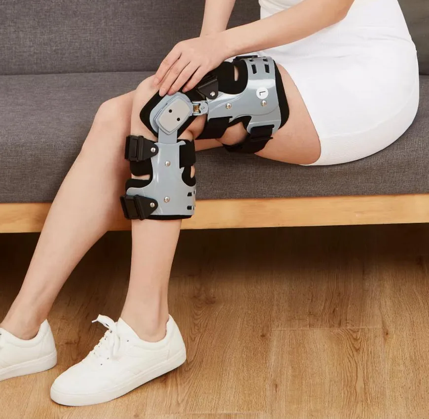Woman seated on a sofa wearing the OA Knee Brace on her left knee