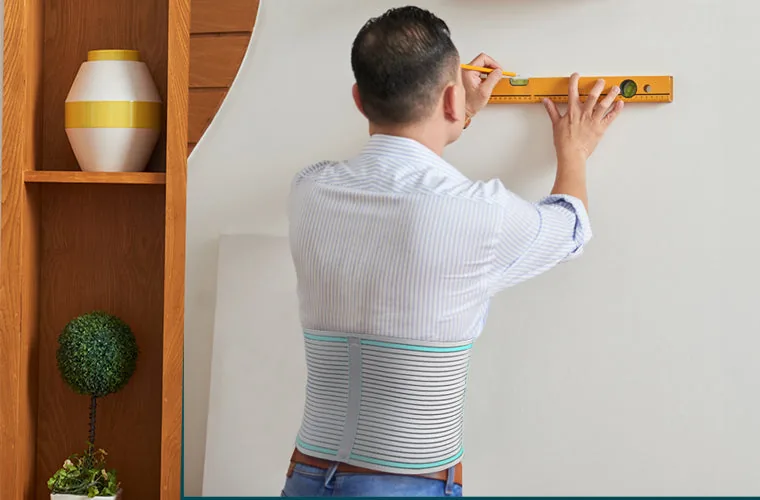 Man in a striped shirt holding a spirit level against a wall, wearing the Tynor Abdominal Support 9 Inch