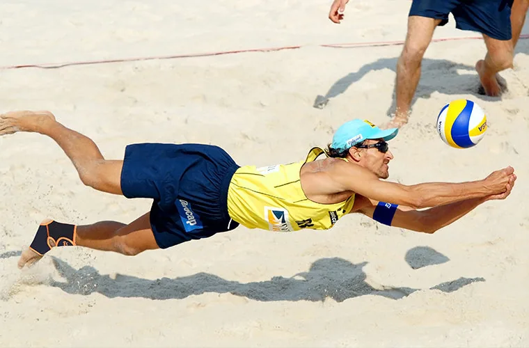 Beach volleyball player diving for the ball on sand, wearing the Tynor Ankle Support (Neo) on his ankle