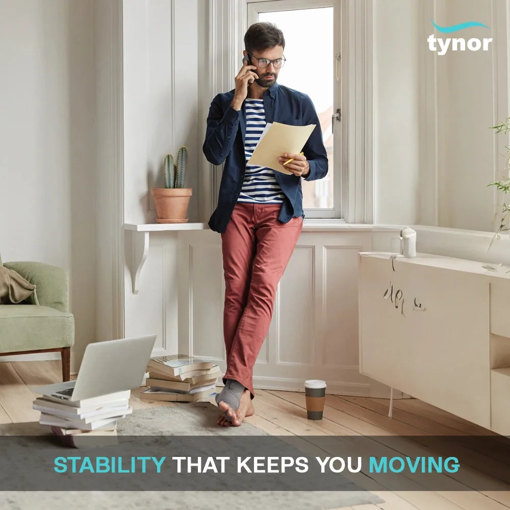 Man standing at home on a phone call, wearing the Tynor Ankle Support (Neoprene)