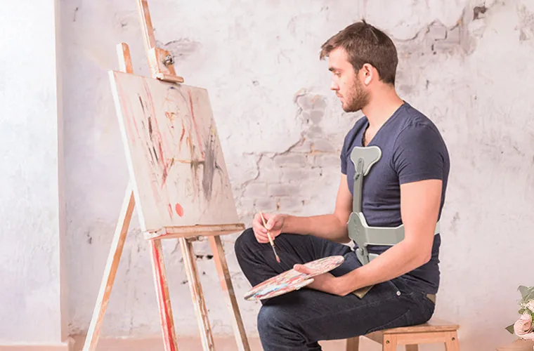 Man painting at an easel while wearing the Tynor Ash Brace (Hyper Extension Brace)