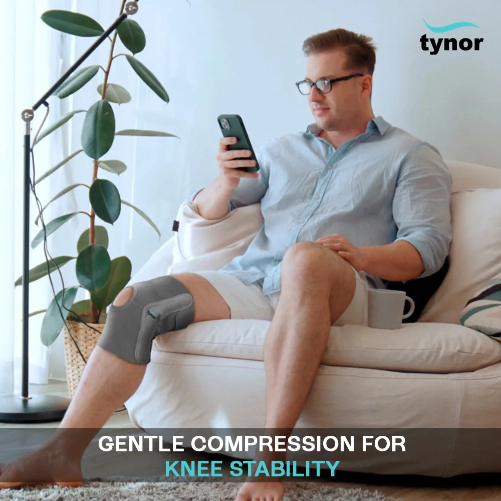 Man sitting on a sofa with his phone while wearing the Tynor Elastic Knee Support