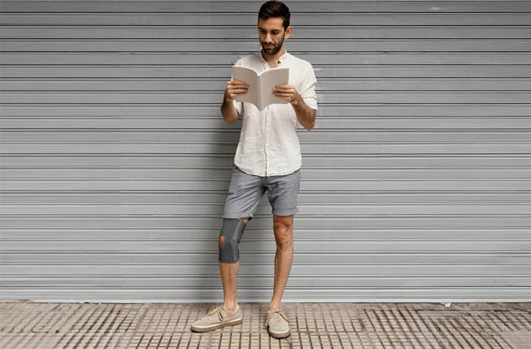 Man reading while standing against a shutter, wearing the Tynor Elastic Knee Support