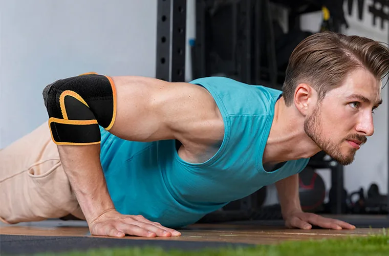 Man doing a push-up while wearing the black and orange Tynor Elbow Wrap (Neo)