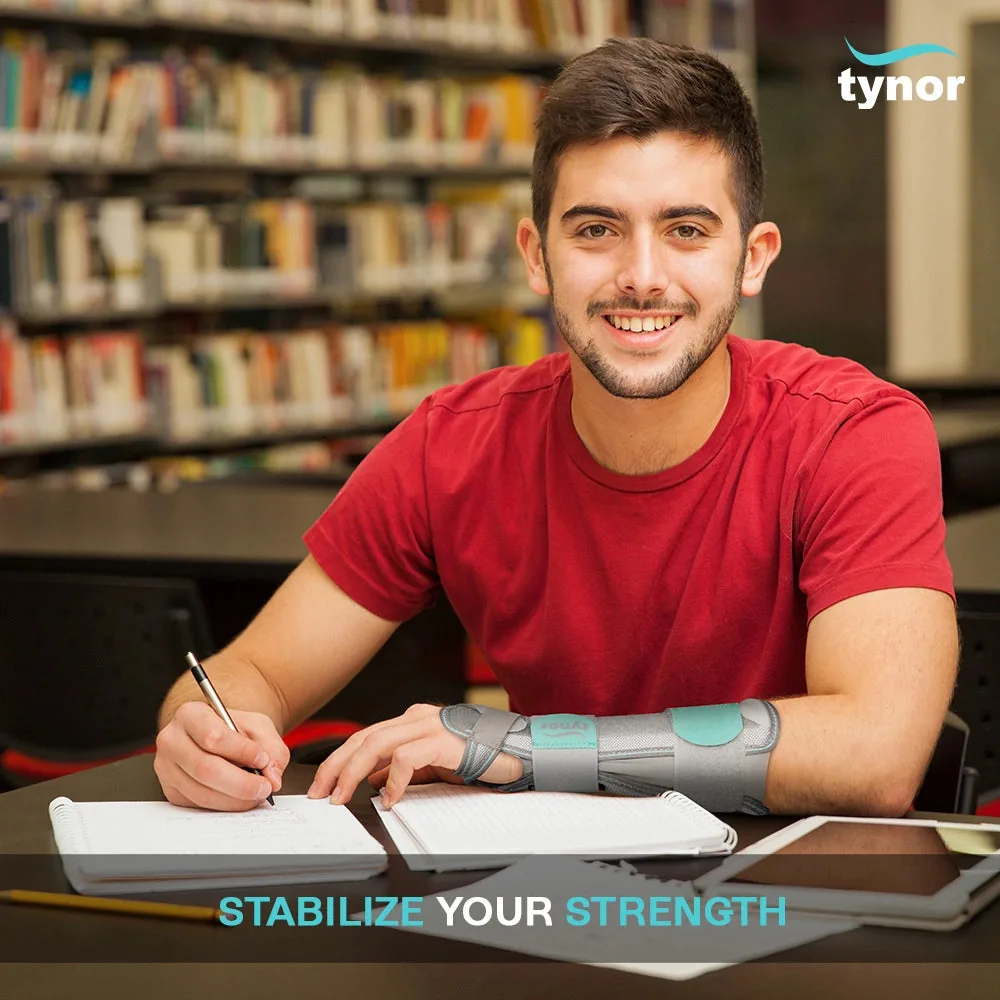 Smiling student in a red T-shirt writing at a library desk, wearing the Tynor Forearm Splint