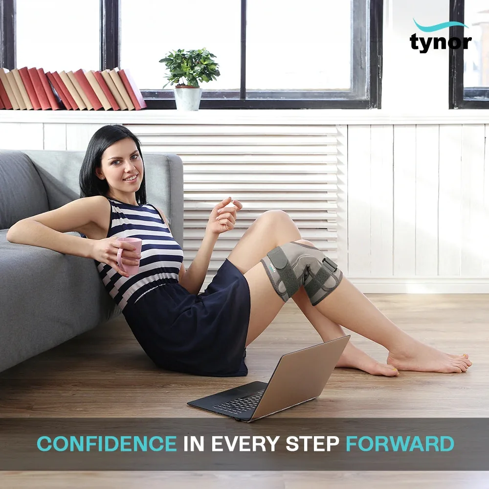 Woman sitting on the floor against a sofa with a mug and laptop, wearing the Tynor Functional Knee Support