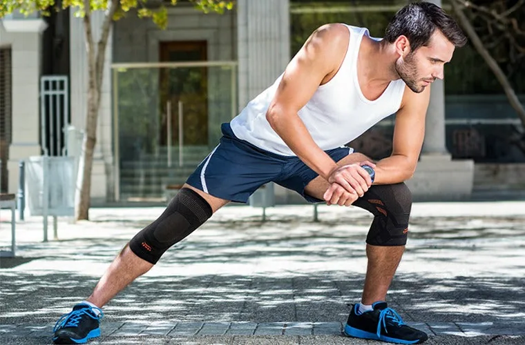 Man in a white vest stretching in a deep lunge outdoors, wearing the Tynor Knee Cap Air Pro on both knees