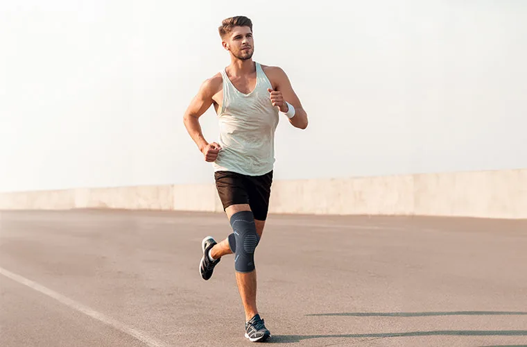 Man in a vest and shorts running on an open road, wearing the Tynor Knee Cap Comfeel