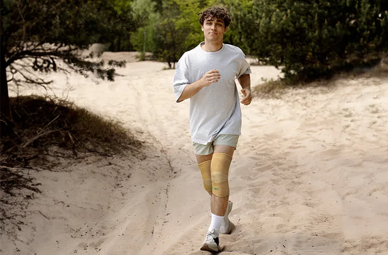 Young man jogging along a sandy path between trees, wearing the beige Tynor Knee Cap on both knees