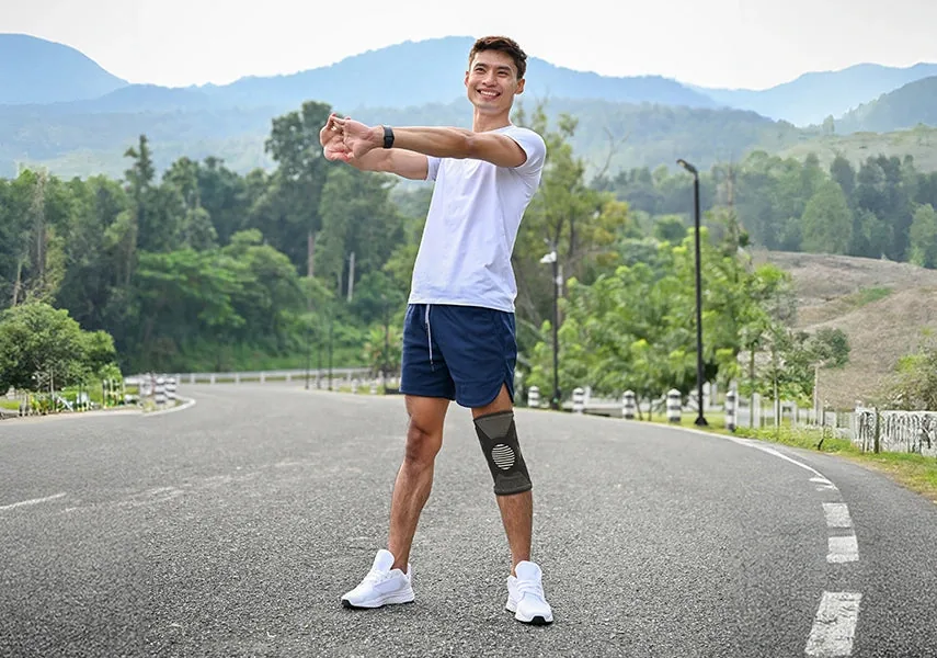 Young man in a white T-shirt stretching his arms on a mountain road, wearing the Tynor Knee Cap With Patellar Ring