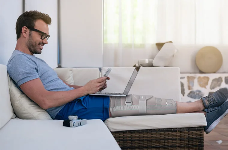 Man using a laptop on a sofa with his leg in the Tynor Knee Immobiliser 19 in