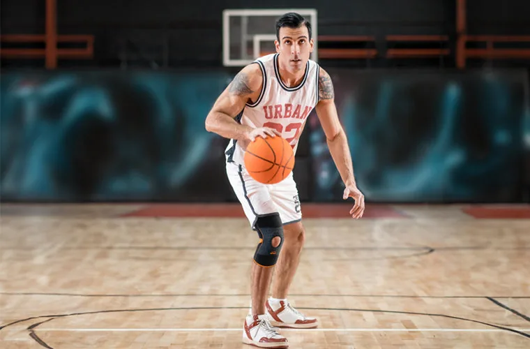 Basketball player dribbling on an indoor court, wearing the black and orange Tynor Knee Wrap (Neo)