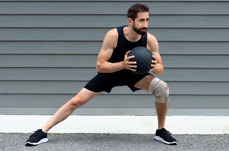 Man in a black vest doing a side lunge with a medicine ball, wearing the Tynor Knee Wrap (Neoprene)