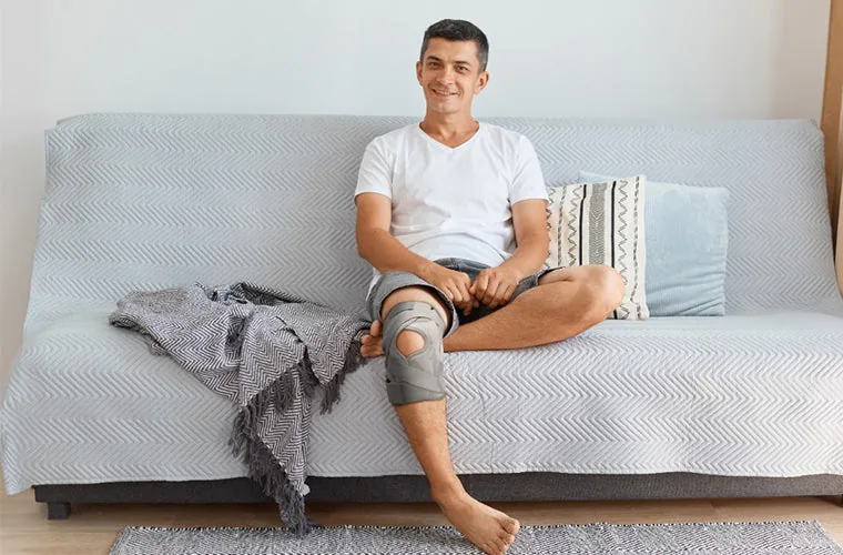 Man sitting on a sofa wearing the grey Tynor OA Knee Support (Neoprene)