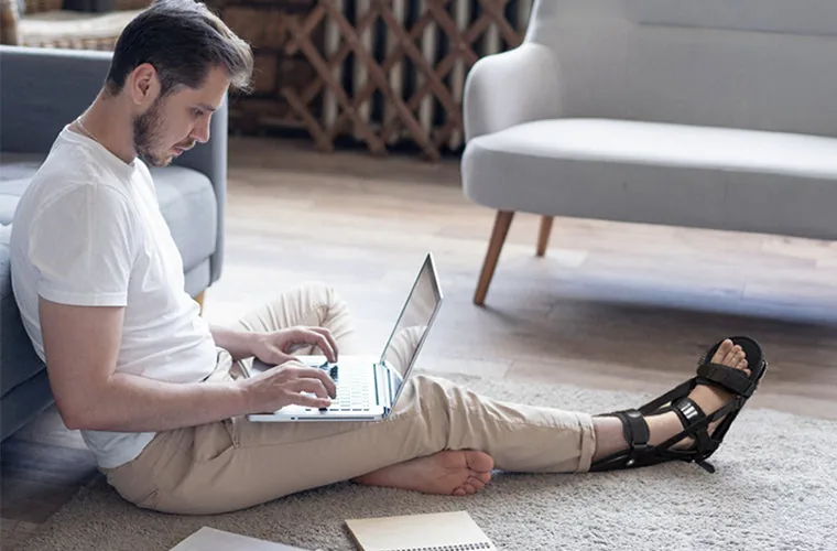 Man working on a laptop on the floor, wearing the Tynor PF Night Splint Derotation