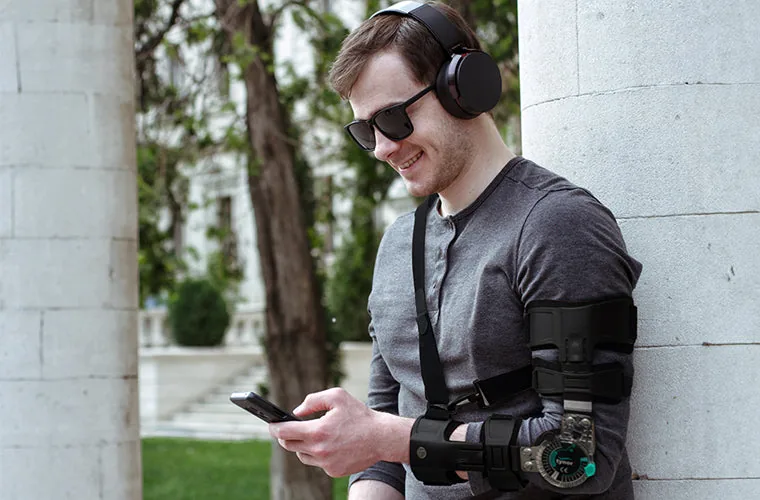 Man with headphones checking his phone while wearing the Tynor R.O.M. Elbow Brace