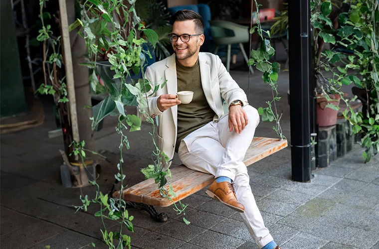 Man in a cream blazer seated on a garden bench among hanging plants, lifestyle scene for the Tynor Scrotal Support