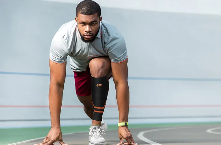 Sprinter in the starting position wearing the black and orange Tynor Shin & Calf Support Air Pro