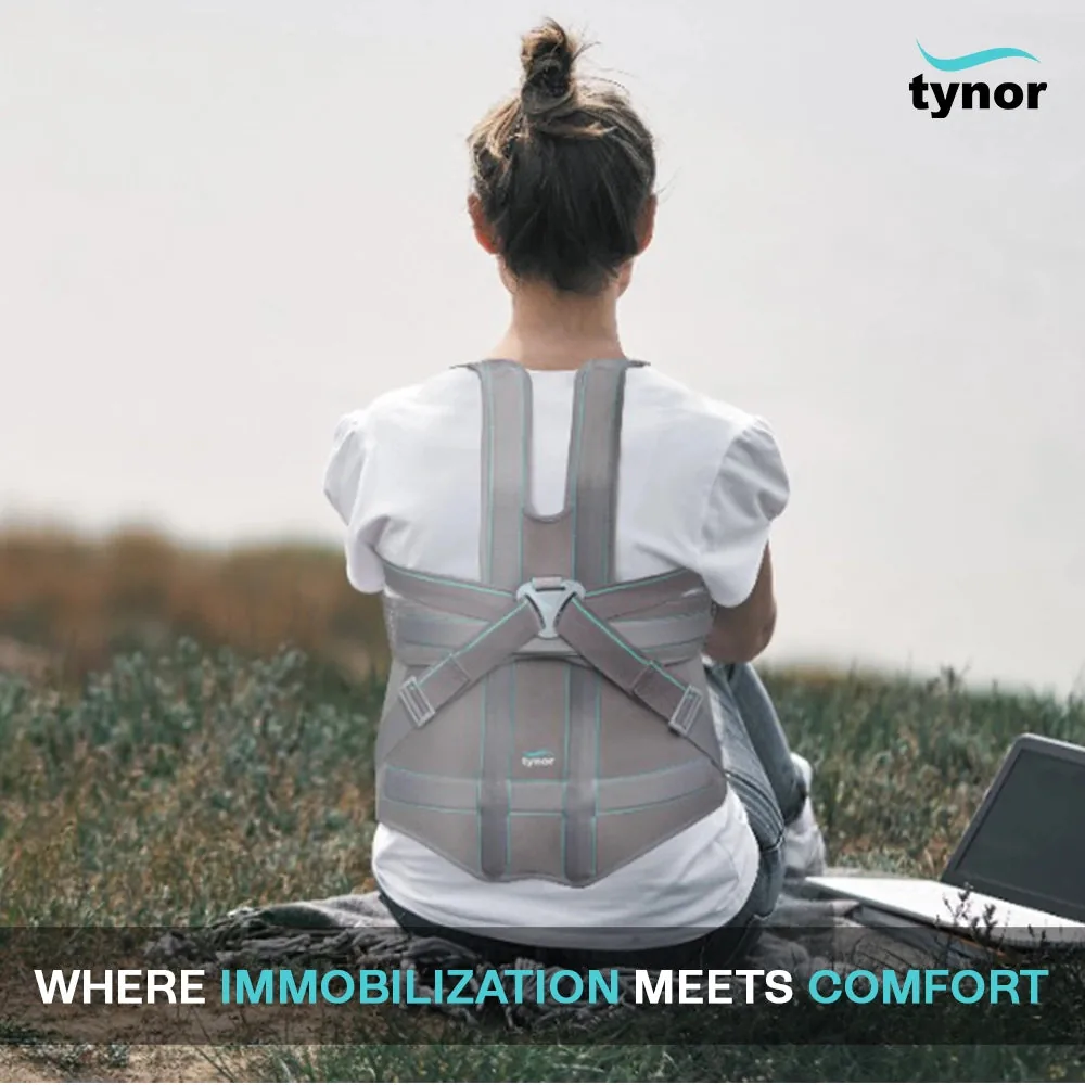 Woman with a hair bun seated outdoors on grass next to a laptop, wearing the Tynor Taylor's Brace Long