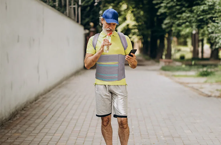 Bearded man in a blue cap drinking water on a tree-lined path, the Tynor Taylor's Brace Long fastened at the front