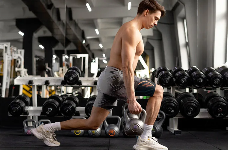 Man doing a lunge with kettlebells in a gym, wearing the black and orange Tynor Thigh Support Air Pro
