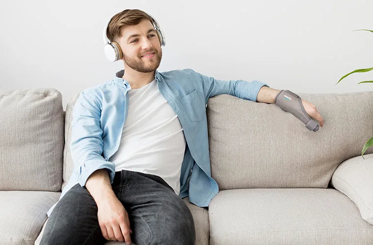 Smiling man in headphones relaxing on a sofa, wearing the Tynor Thumb Spica Splint on his hand
